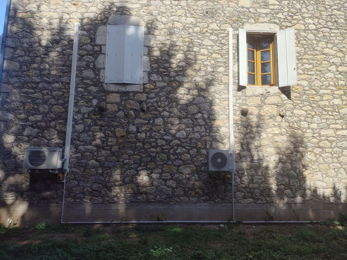 Klimaanlage an einem Steinhaus – Gesamtansicht, unauffälliges Gerät am Fuß der Fassade
